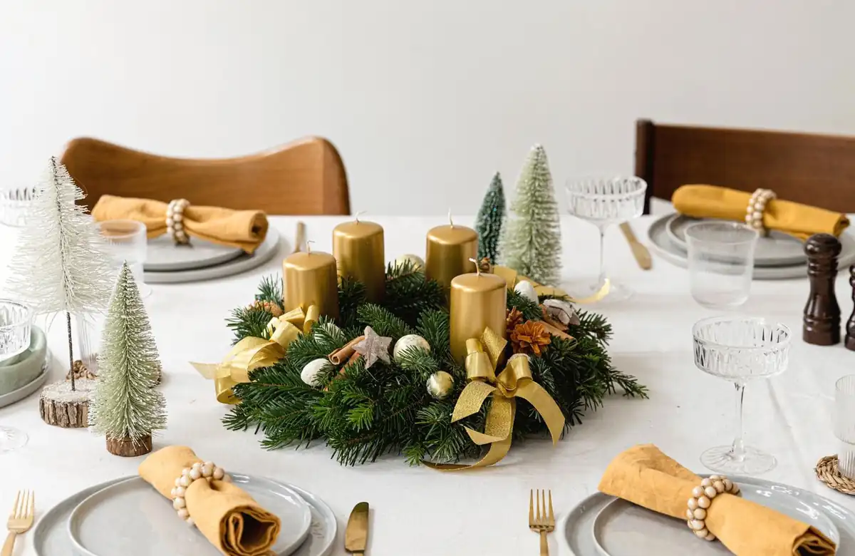 Handgebundener Adventkranz mit goldenen Kerzen und Goldband auf einer festlich gedeckten Tafel
