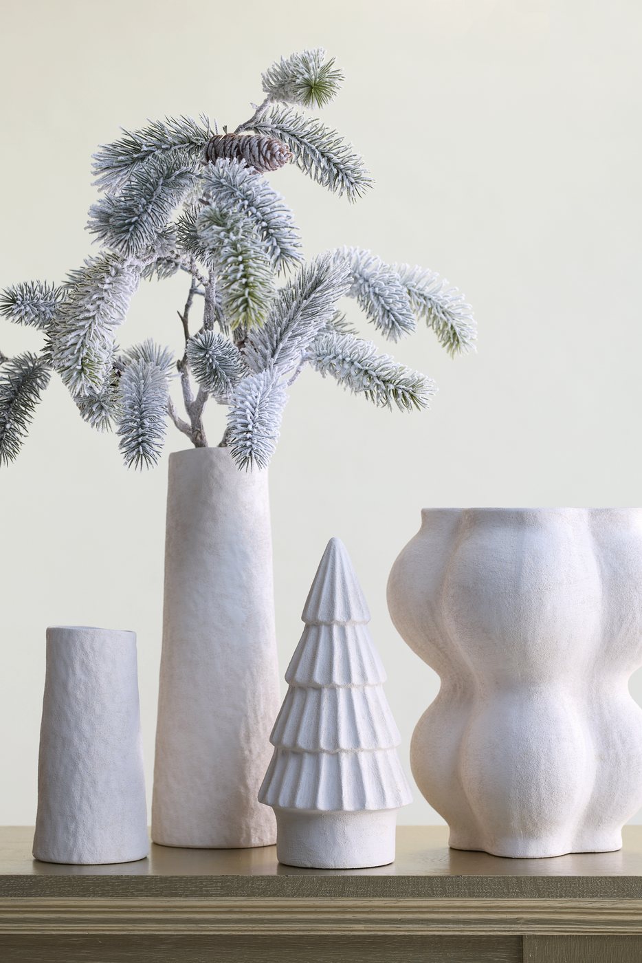 Weiße Keramikvasen mit beschneiten Kiefernzweigen und einem Keramikbaum