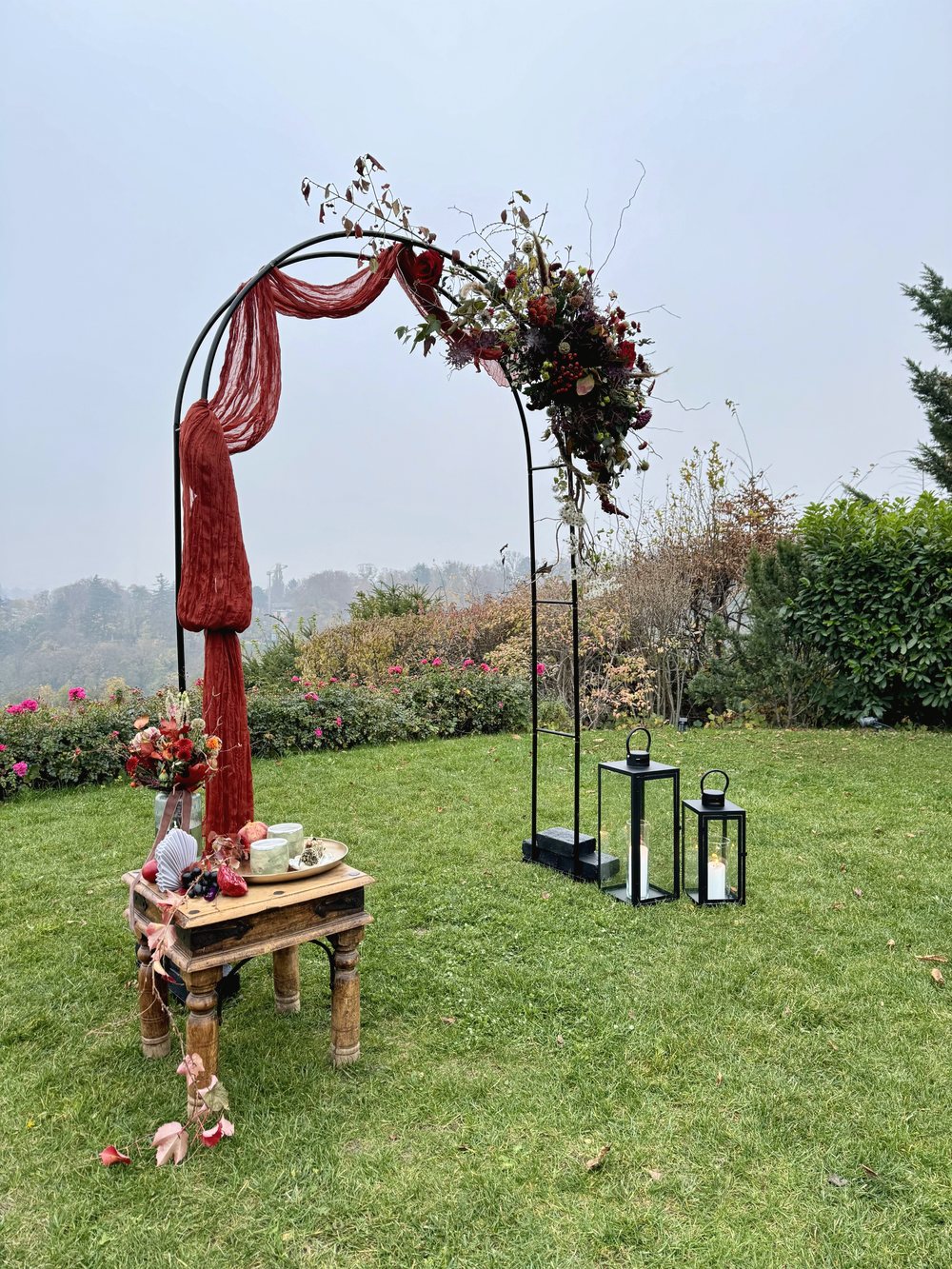 Hochzeitsbogen mit Bordeaux-Stoff und Blumen in Orange im Garten
